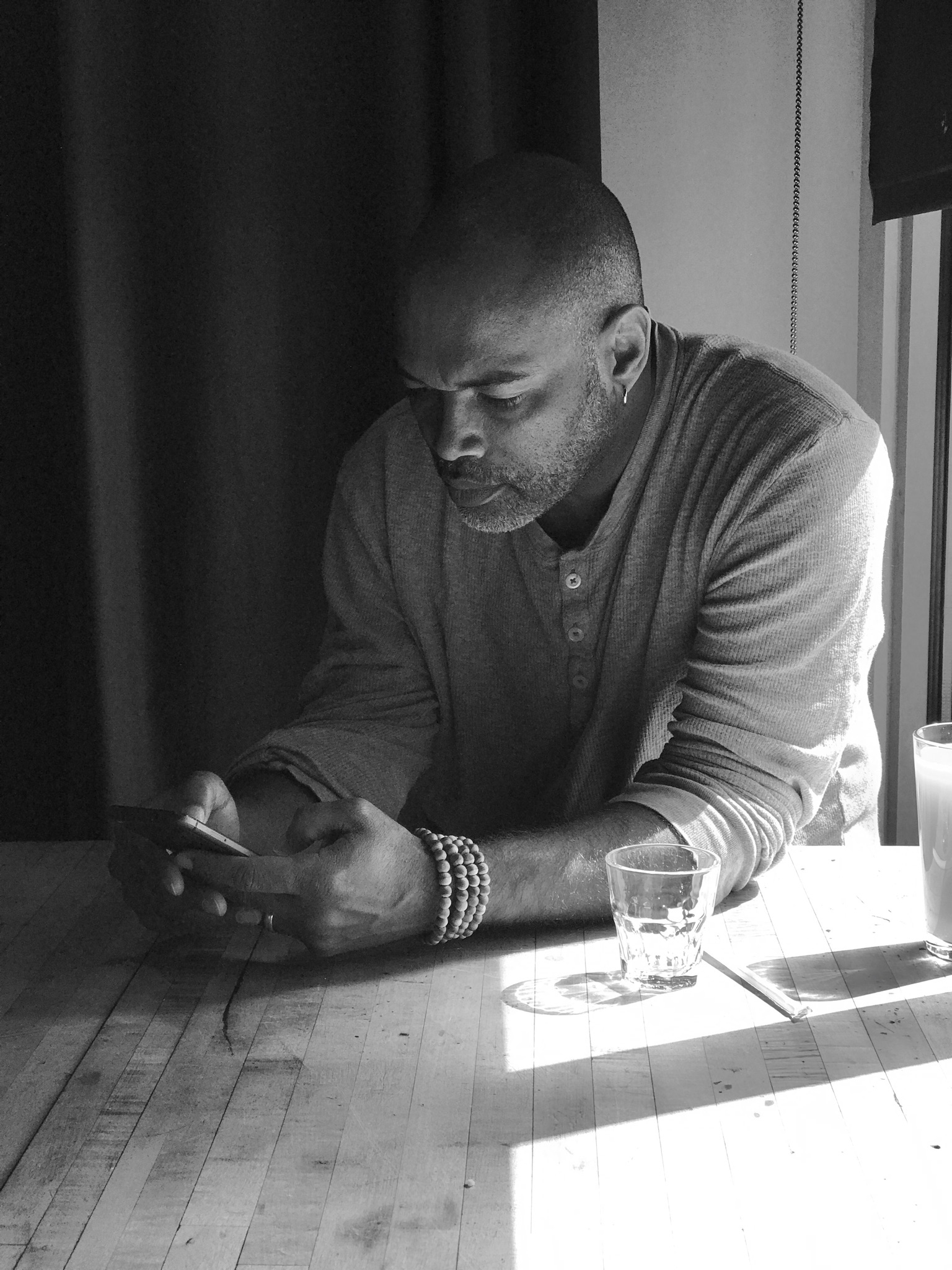 Black and white photo of me sitting at a table looking at something on my phone.